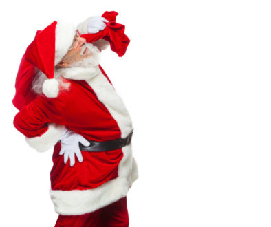 Christmas. Santa Claus is suffering from back pain and holds a red bag with gifts on his back. Isolated on white background.