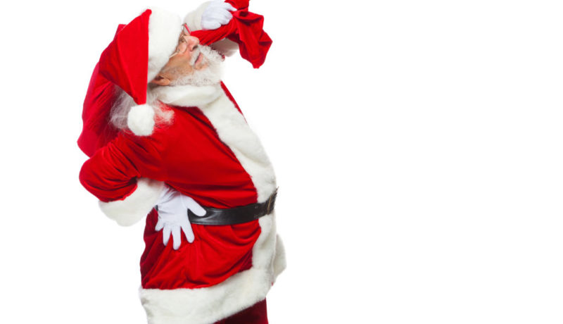 Christmas. Santa Claus is suffering from back pain and holds a red bag with gifts on his back. Isolated on white background.